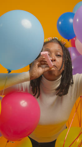 Vertical-Video-Studio-Portrait-Of-Woman-Wearing-Birthday-Headband-Celebrating-With-Balloons-And-Party-Blower-1